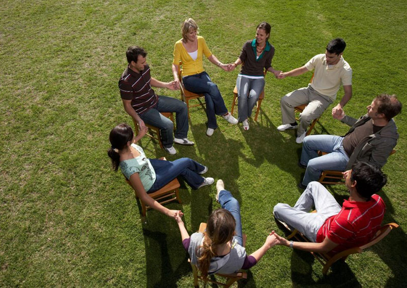 A group of people sitting in the grass holding hands.