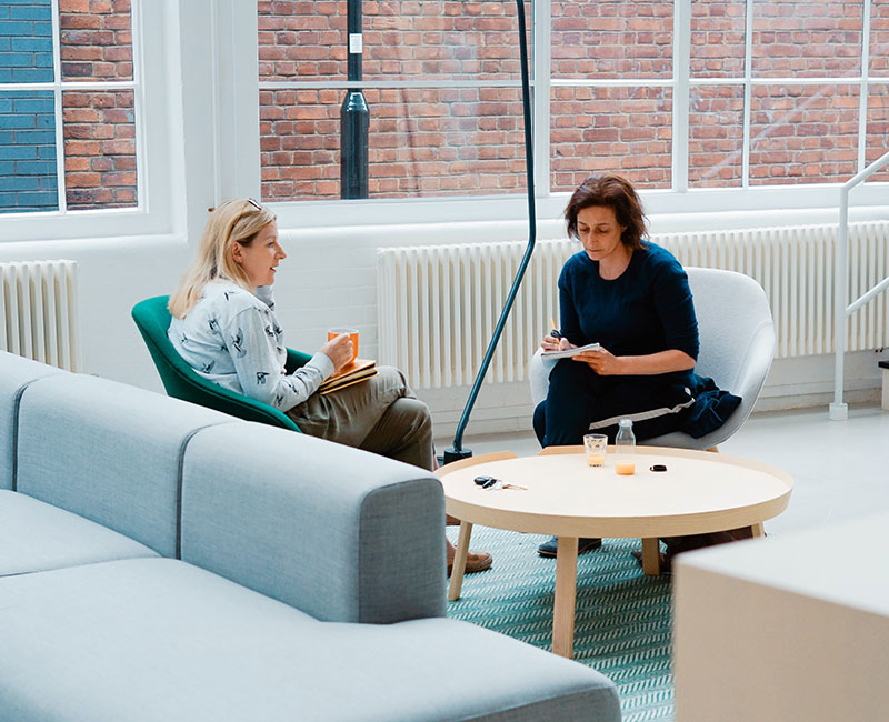 Two women sitting on a couch in front of a window.